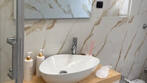 Une salle de bain moderne avec un pare-baignoire en marbre, un grand miroir, un lavabo sur colonne et une baignoire.