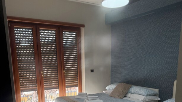 Une chambre avec deux lits, une grande fenêtre avec stores, un luminaire au plafond et un tapis à motifs.