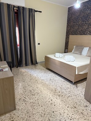 Una habitación de hotel con una cama, una mesita de noche de madera, un escritorio y un suelo estampado.
