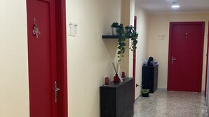 Un couloir avec des portes rouges, un comptoir d’accueil agrémenté de plantes et un sol carrelé.
