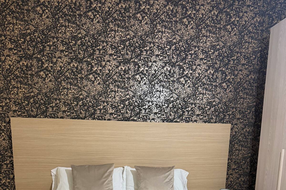 Una cama grande con cabecera de madera, dos almohadas blancas y dos toallas enrolladas.