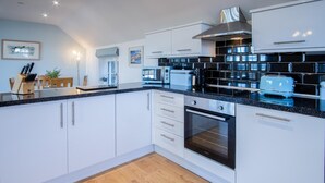 A modern kitchen with white cabinets, black countertops, and a built-in oven. - Caldey View Cottage - 1 Bedroom - Penally (Tenby)