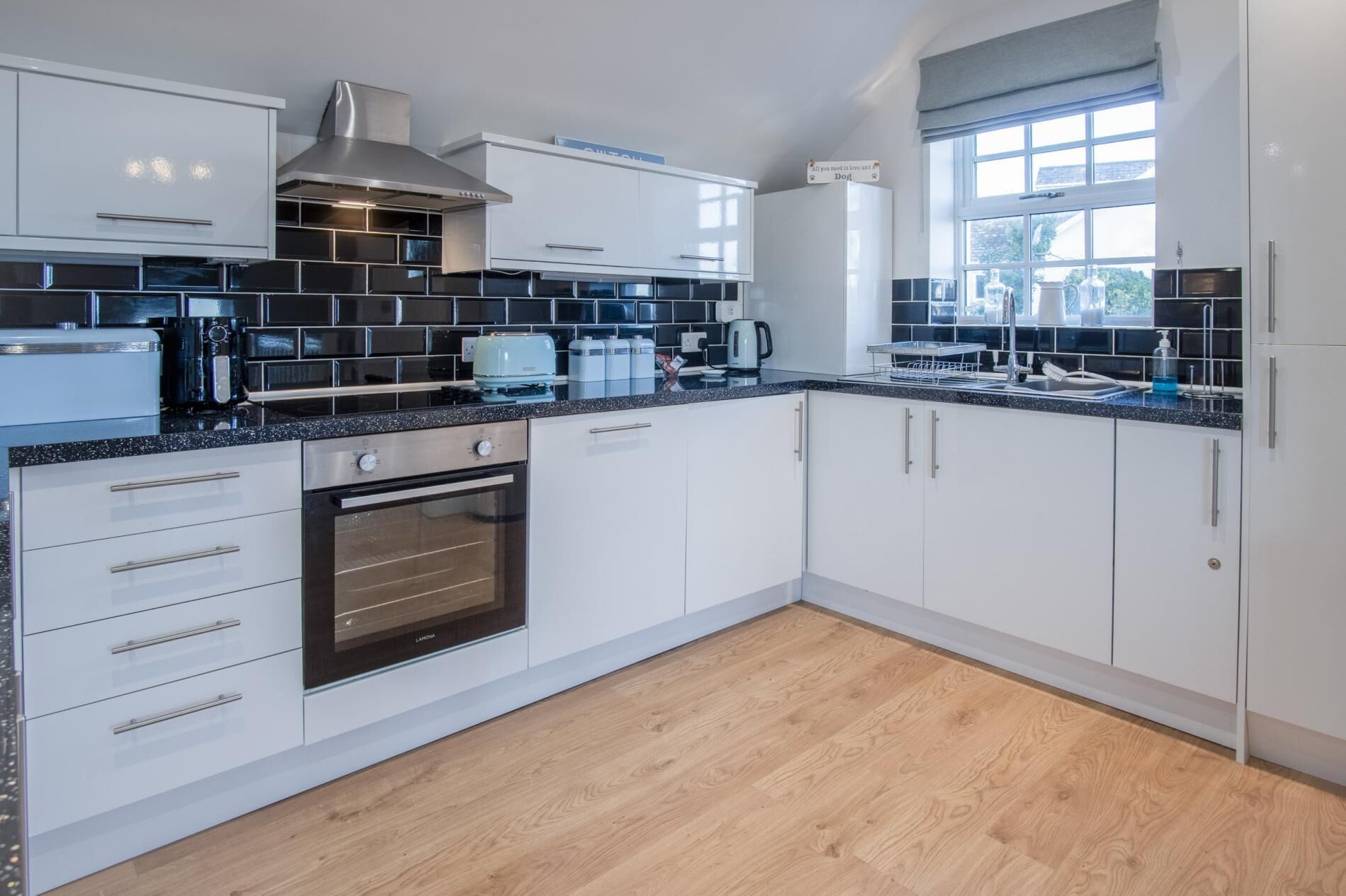 A modern kitchen with white cabinets, a stainless steel range hood, a built-in oven, and a window providing natural light.