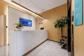 A reception area with a reception desk, a digital screen, a potted plant, and a wall-mounted sign. - Home Inn Huayi Select Collection Hotel (Tongzhou)