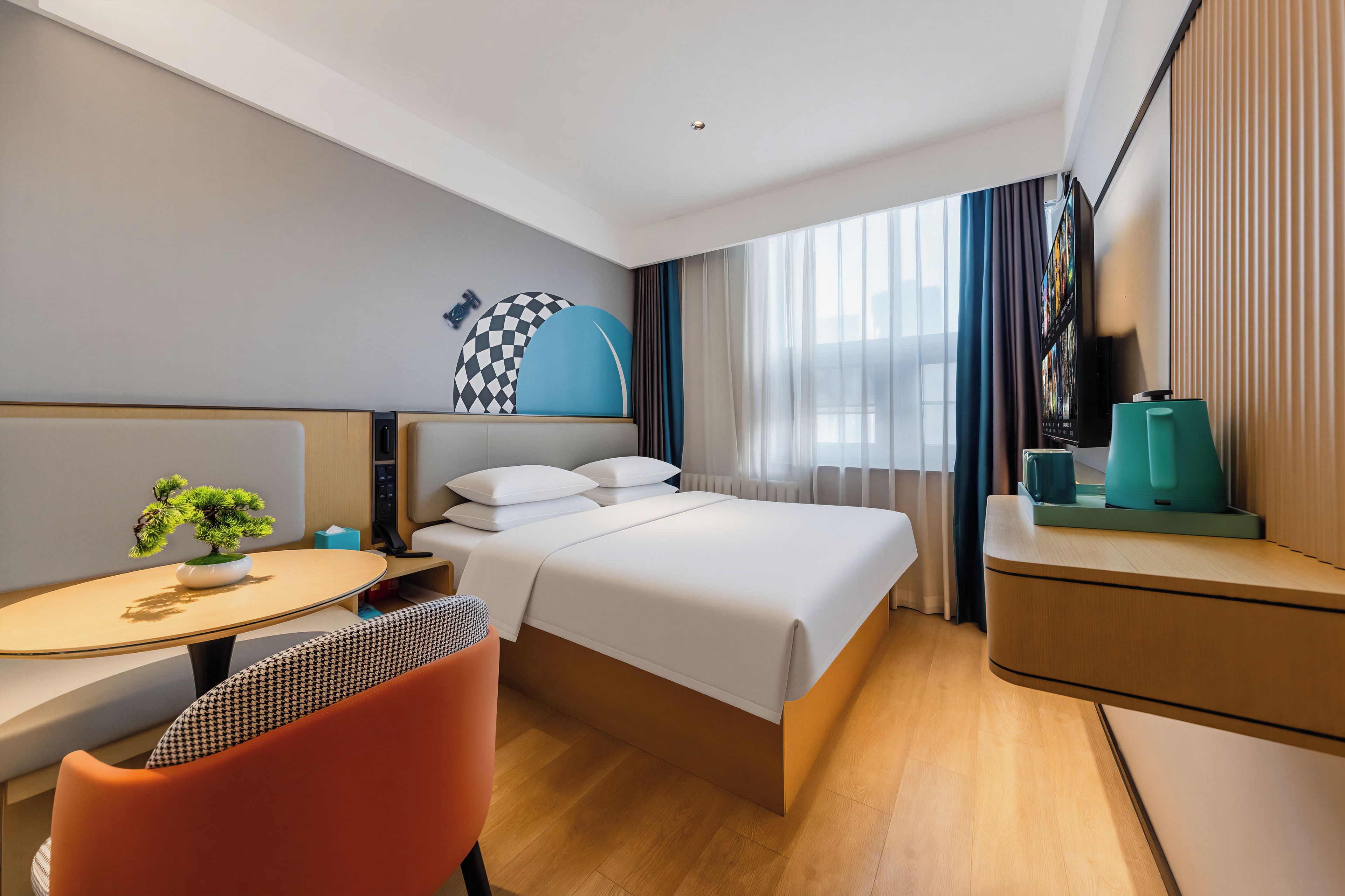 A hotel room with a bed, a desk with a chair, a small table with a plant, and a TV on a stand.