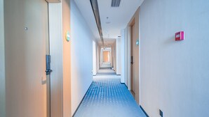 Ein Hotelgang mit blauem Teppich, Türen an beiden Seiten und einem Rauchmelder an der rechten Wand.