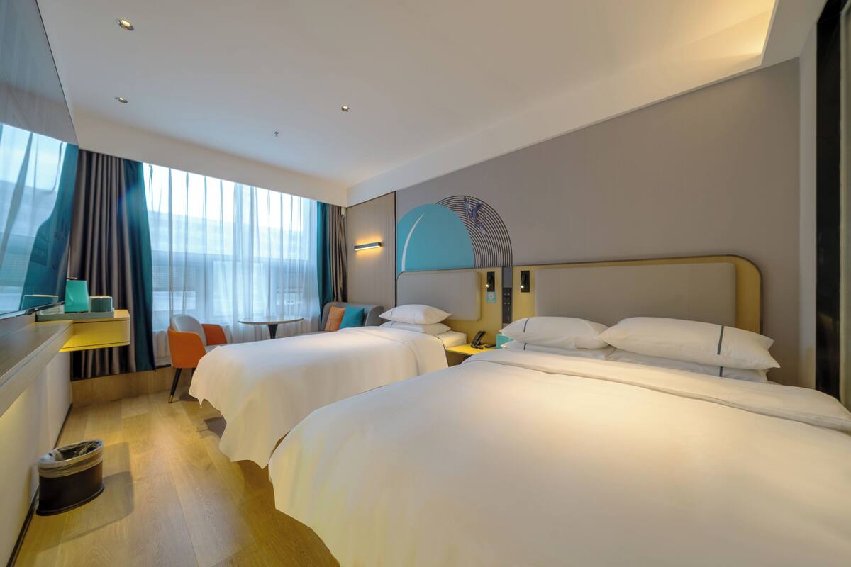 A hotel room with two beds, a desk, a chair, and a large window with curtains.