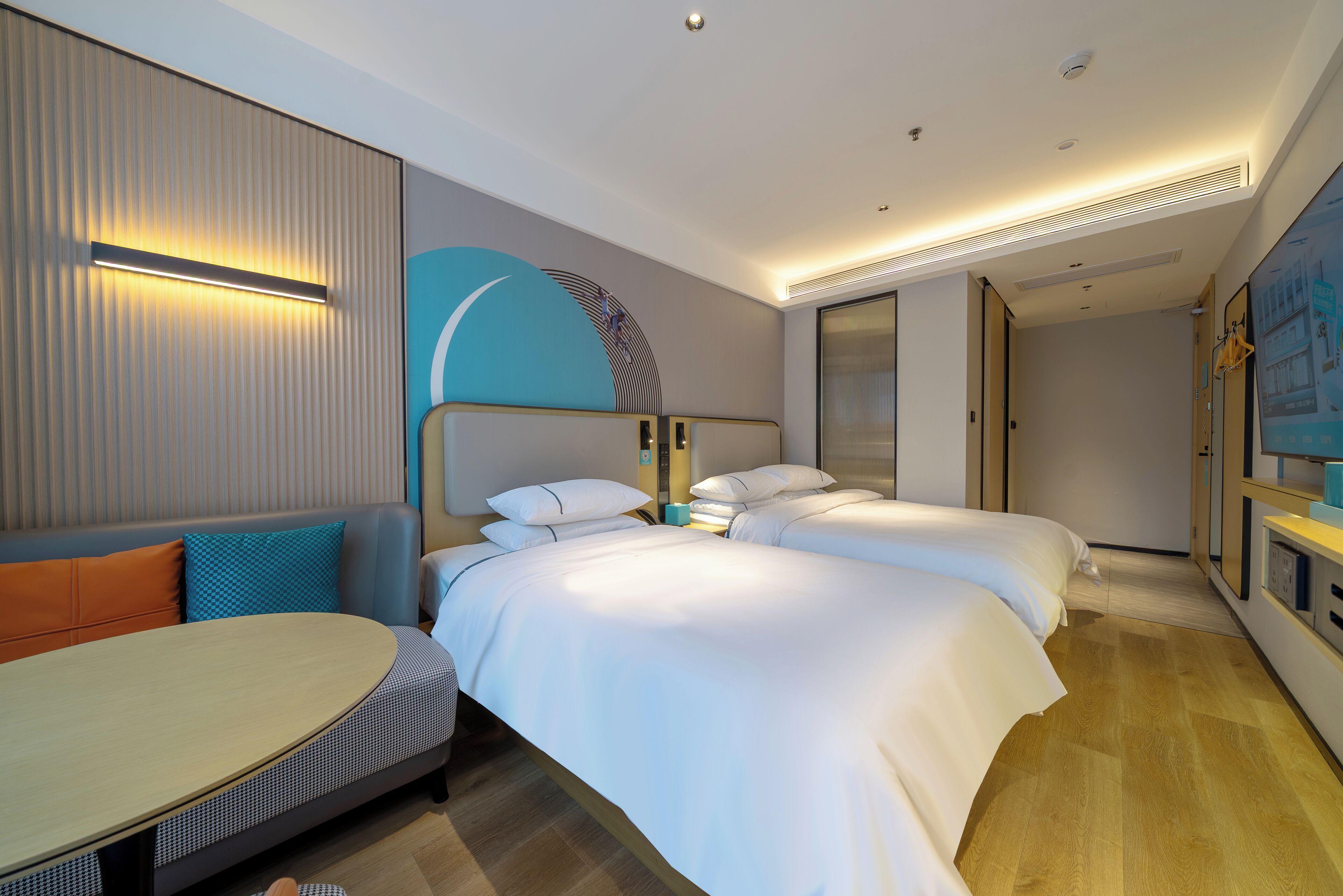 A modern hotel room with a sofa, two beds, a small table, and a large window.