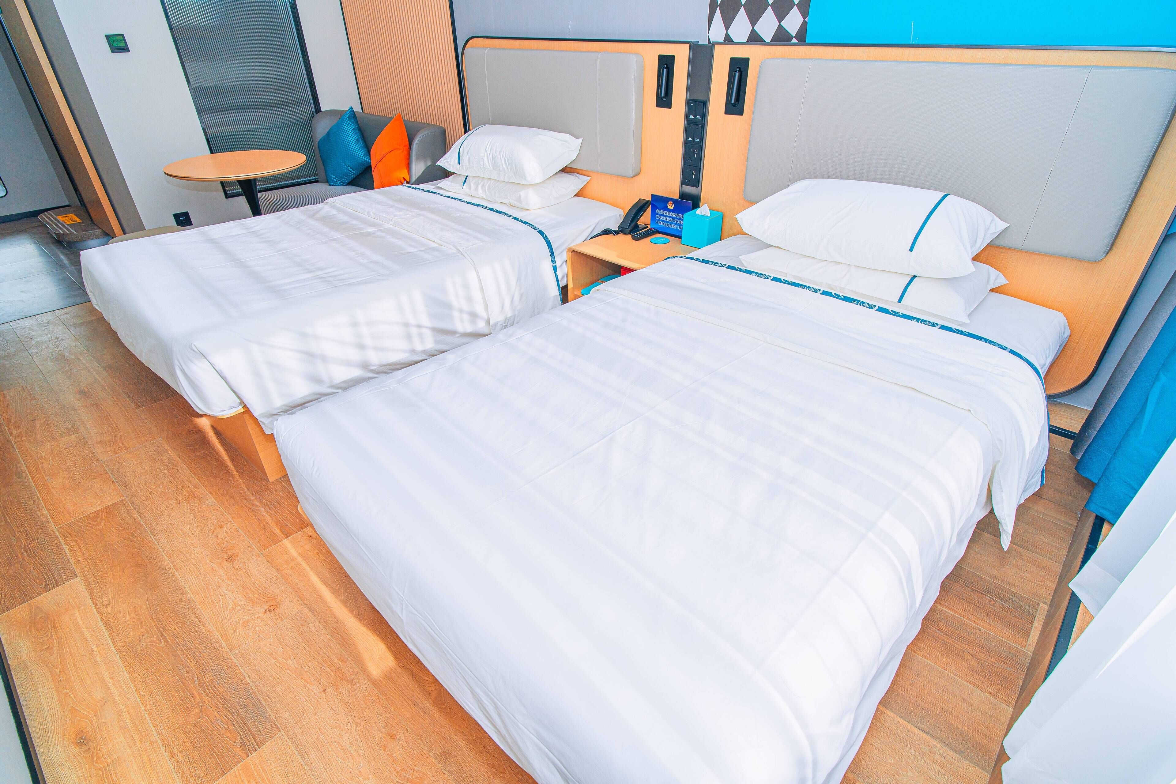 A hotel room with two beds, a small table, and a nightstand with a phone and tissues.