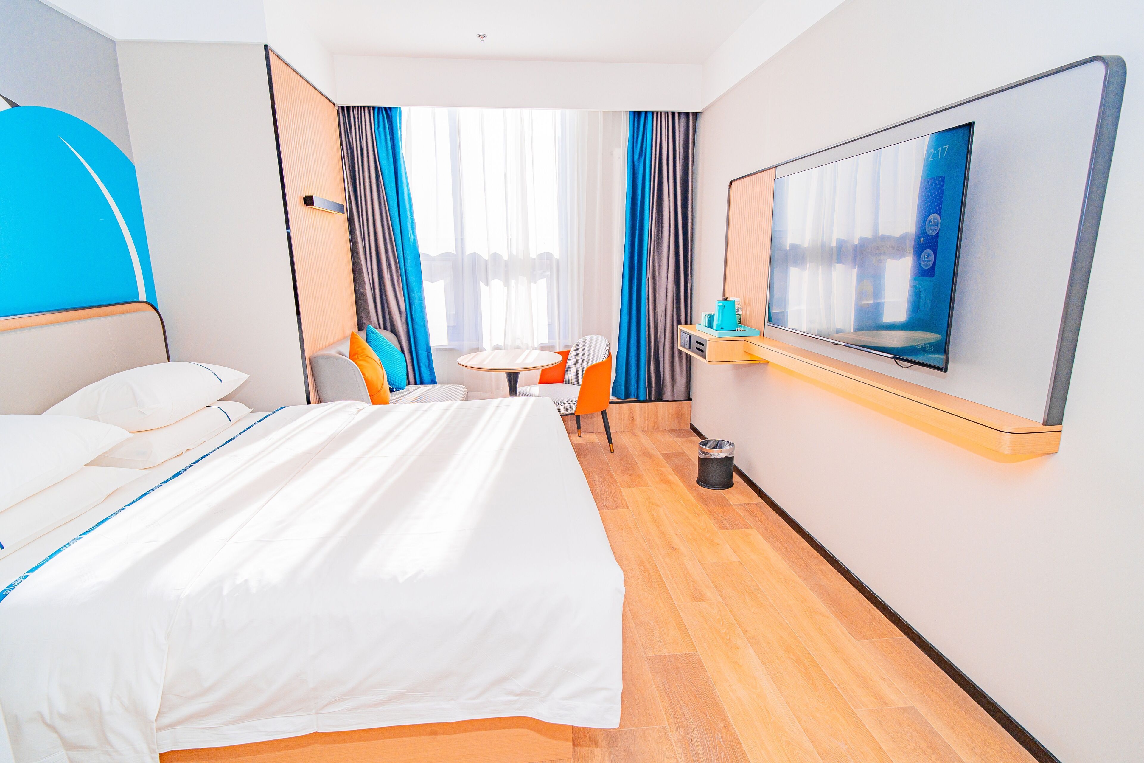 A hotel room with a bed, a small table, two chairs, a TV, and a window with curtains.