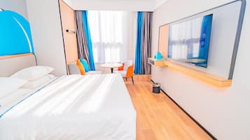 A hotel room with a bed, a small table, two chairs, a TV, and a window with curtains.