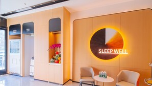 A modern hotel lobby with a 'SLEEPWELL' sign, seating area, and a reception desk with a plant. - Home Inn Huayi Select Collection Hotel  (Tongzhou)