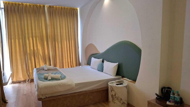 A hotel room with a bed, a bedside table, a lamp, a curtain, and a window. - Palette The Moon Hotel Goa by Sunday 2 (Nerul)