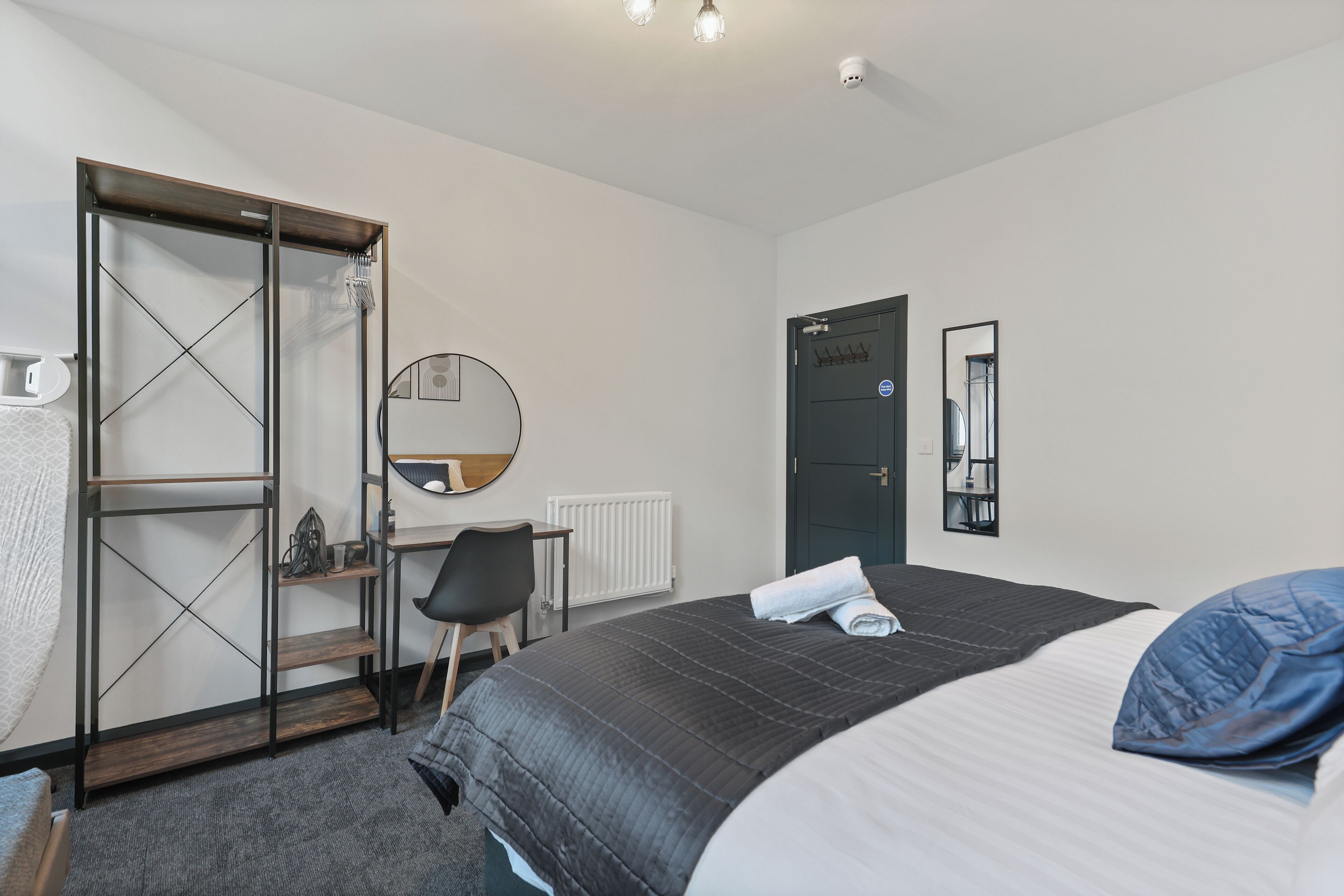 Ein Schlafzimmer mit Bett, Schreibtisch, Stuhl, Kleiderschrank und einer Tür.
