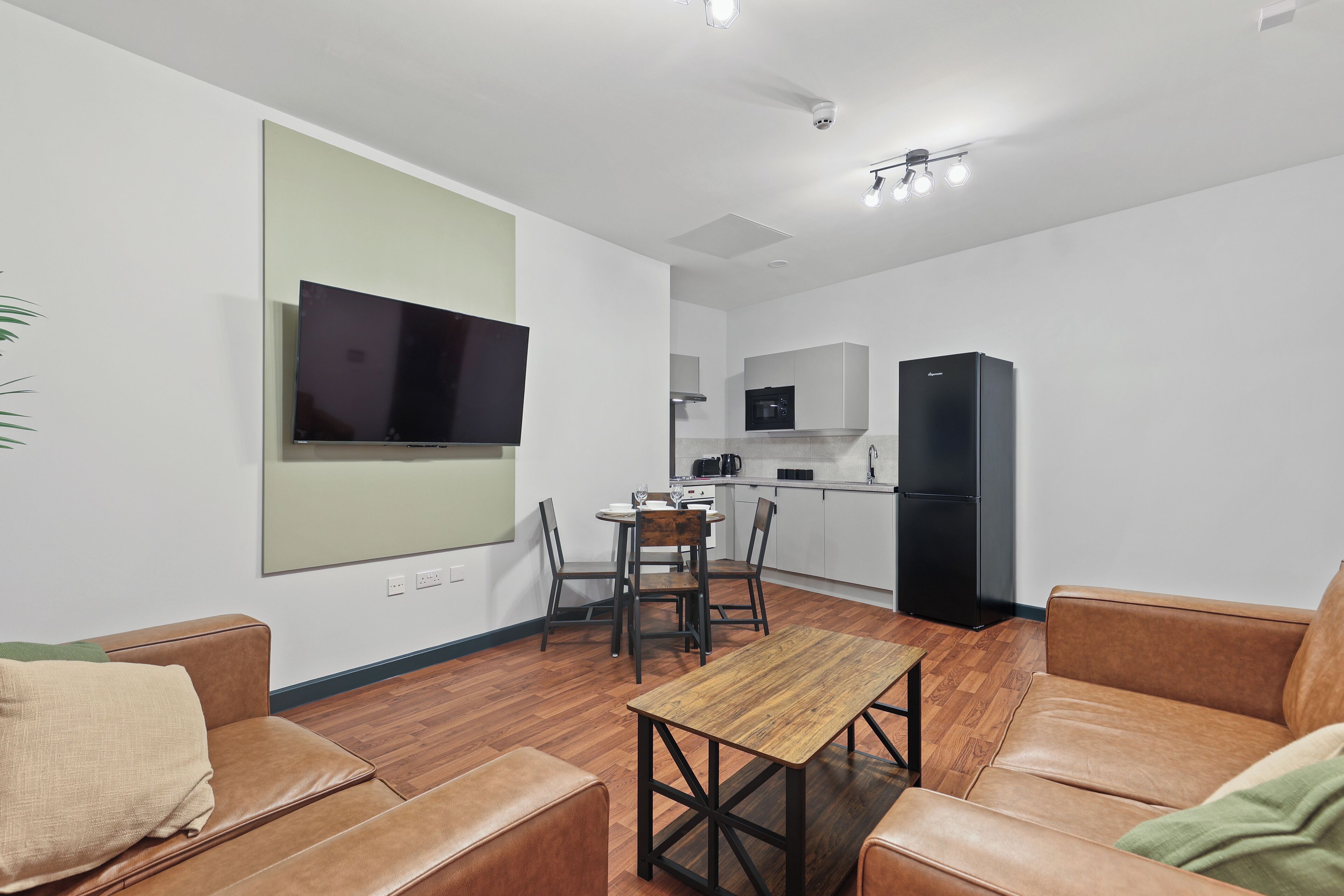 A modern living room with a wooden coffee table, leather sofas, and a flat-screen TV mounted on the wall.
