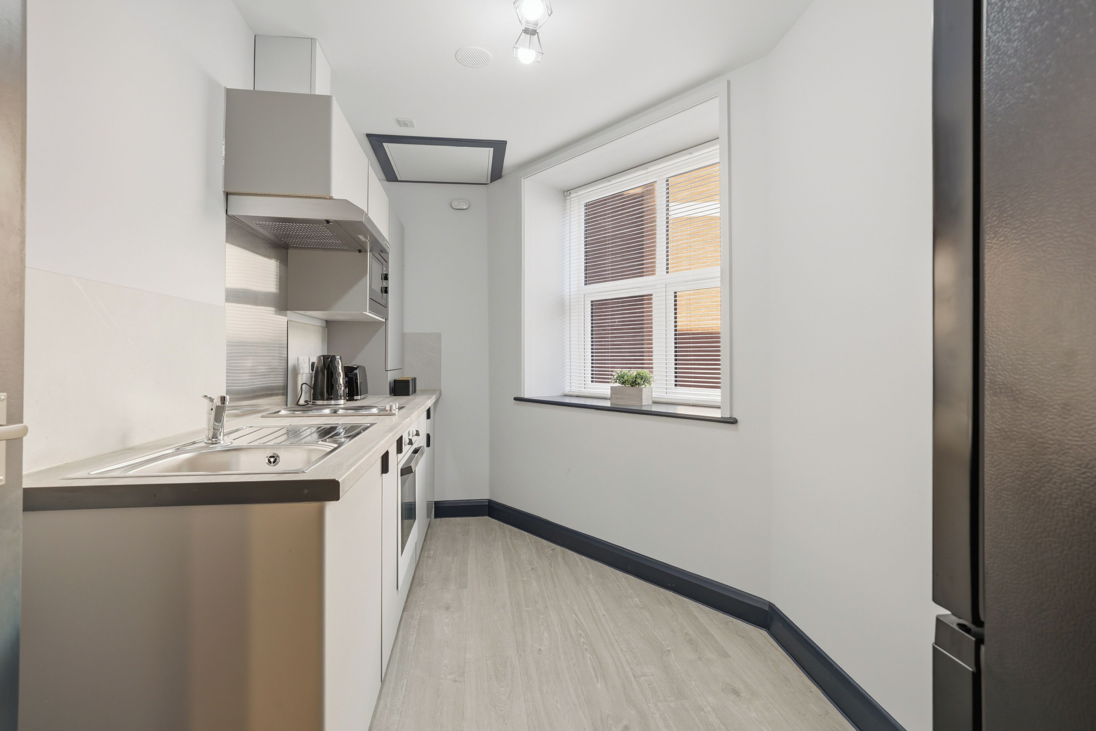 A modern kitchen with a stainless steel refrigerator, a built-in oven, and a window with blinds.