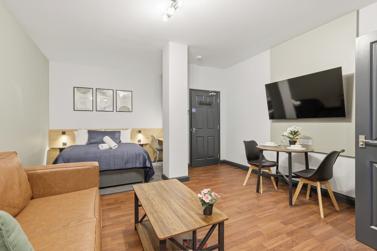 Una habitación de hotel moderna con cama, escritorio, silla, televisor y una pequeña mesa con una flor.
