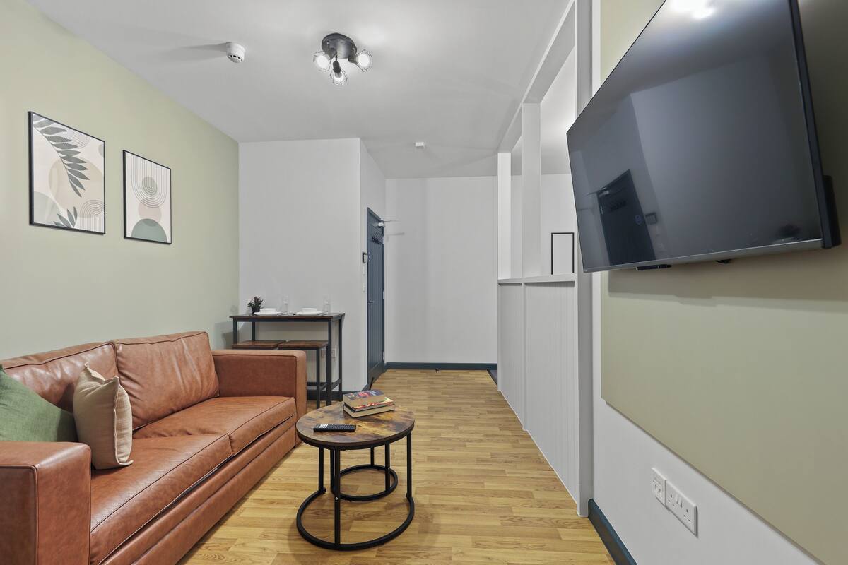 Una sala de estar moderna con un sofá de cuero, una mesa de centro redonda y un televisor de pantalla plana montado en la pared.