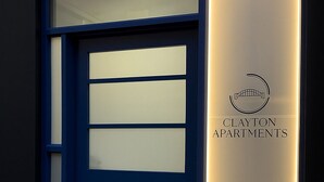 Una porta blu con pannelli di vetro smerigliato e un neon che indica Clayton Apartments.