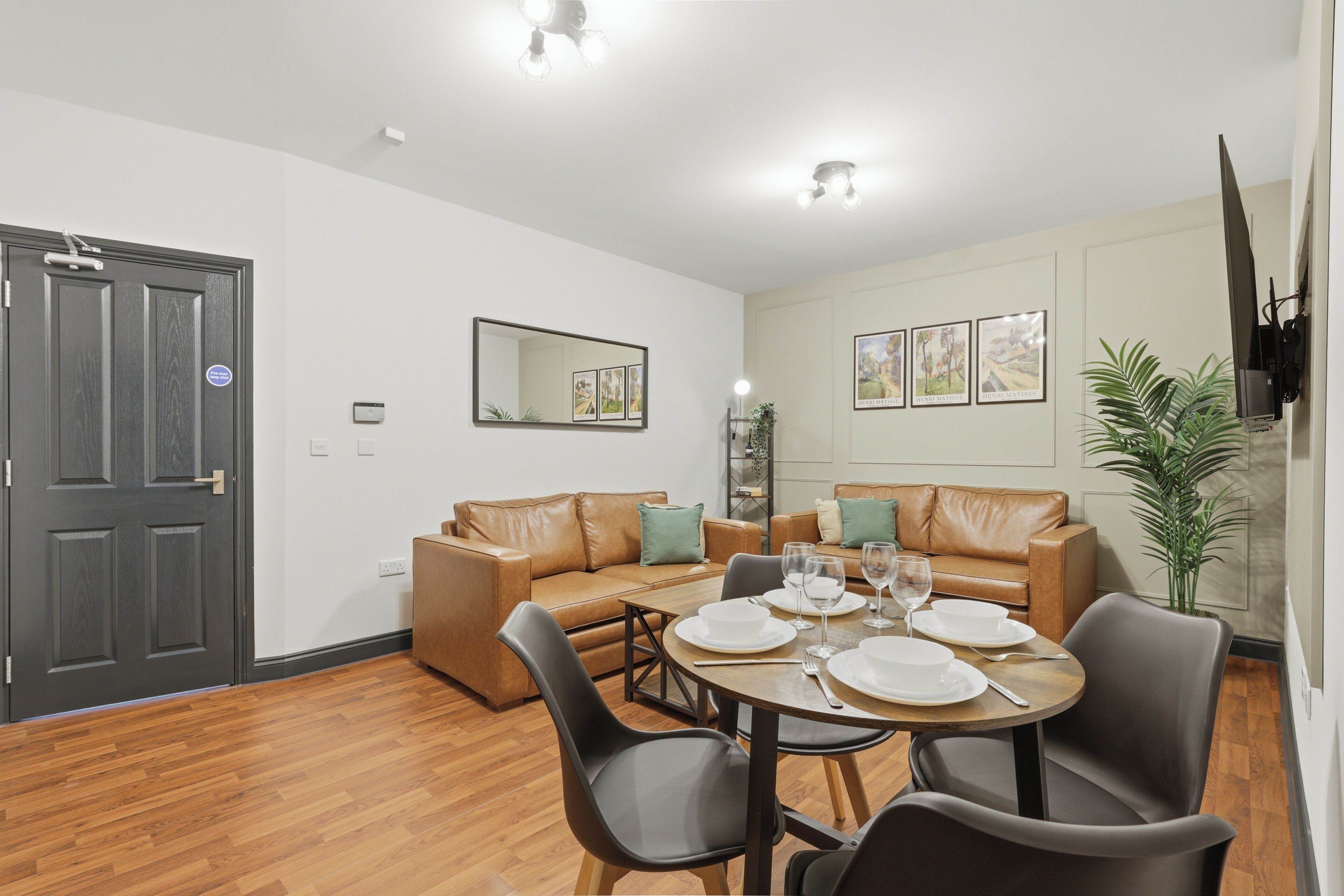Un coin repas avec une table ronde dressée pour quatre personnes, deux canapés et un grand miroir au mur.