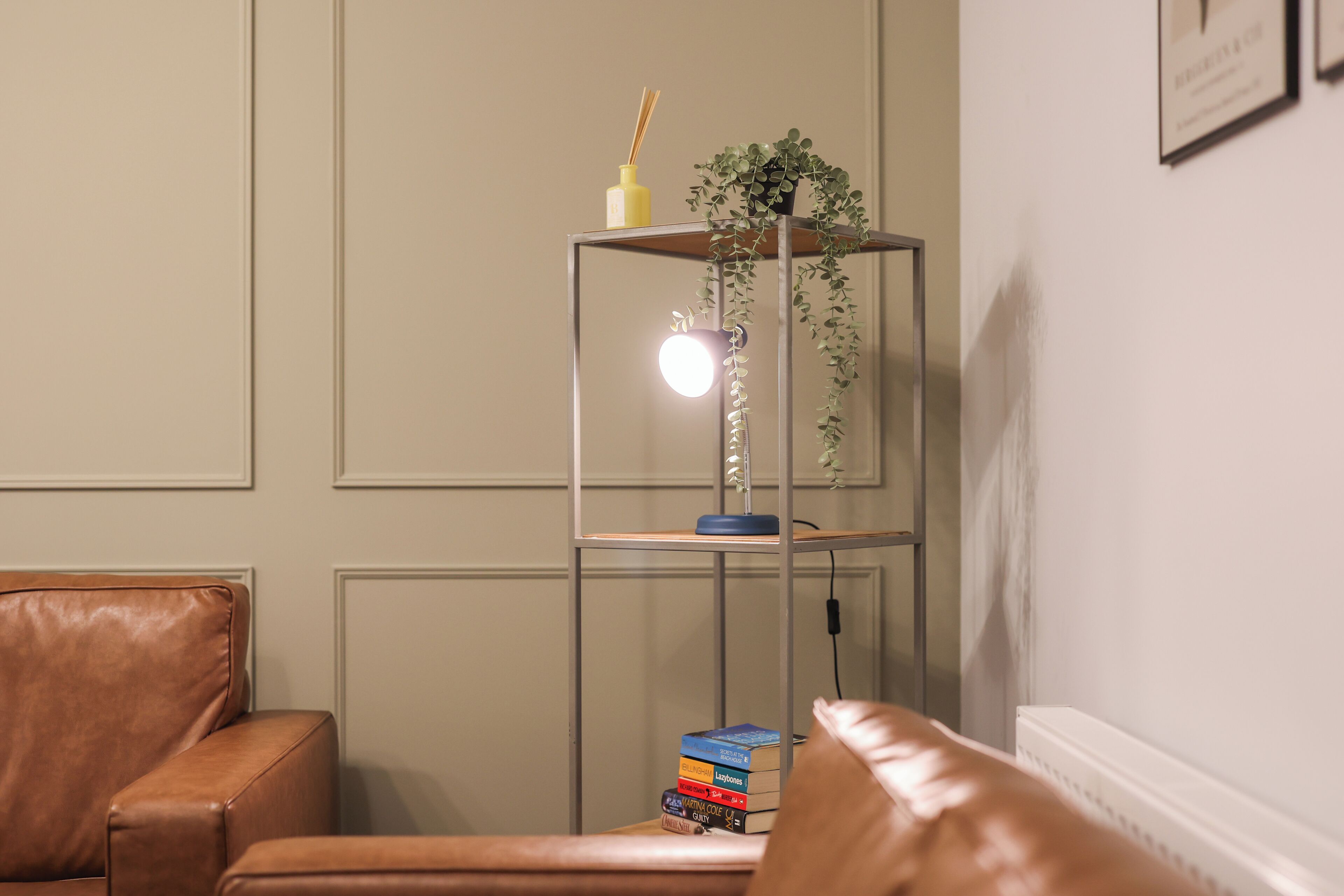 A room with a leather armchair, a glass table with a lamp, a plant, and a stack of books.