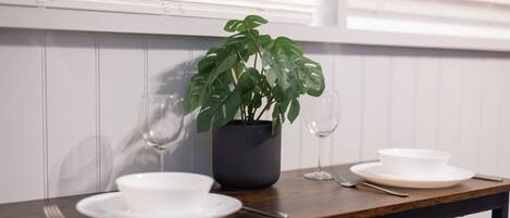 Una mesa de comedor con una planta en maceta, dos copas de vino y un juego de vajilla blanca.
