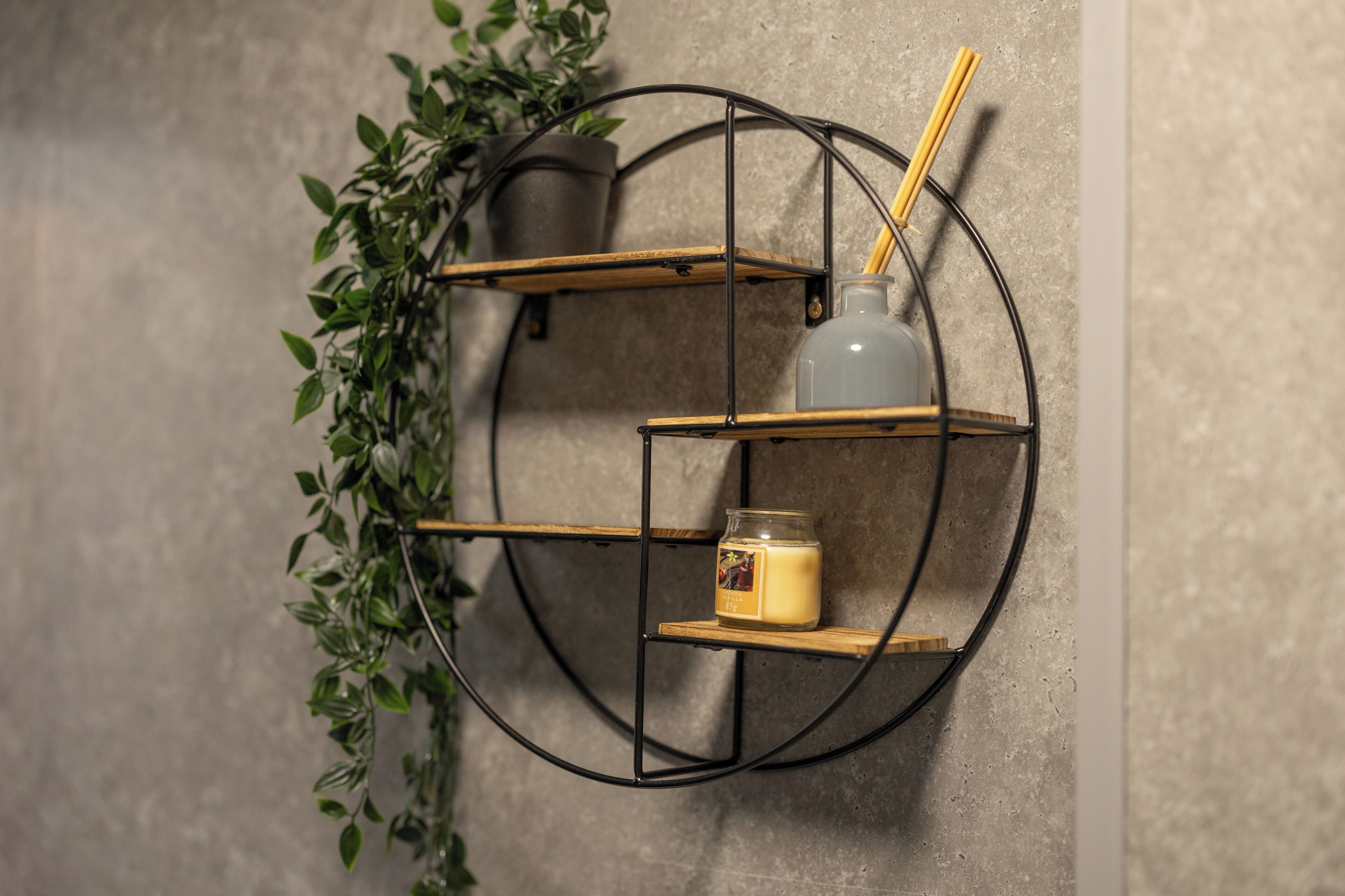 A circular metal shelf unit with a candle and a jar on it, surrounded by greenery.