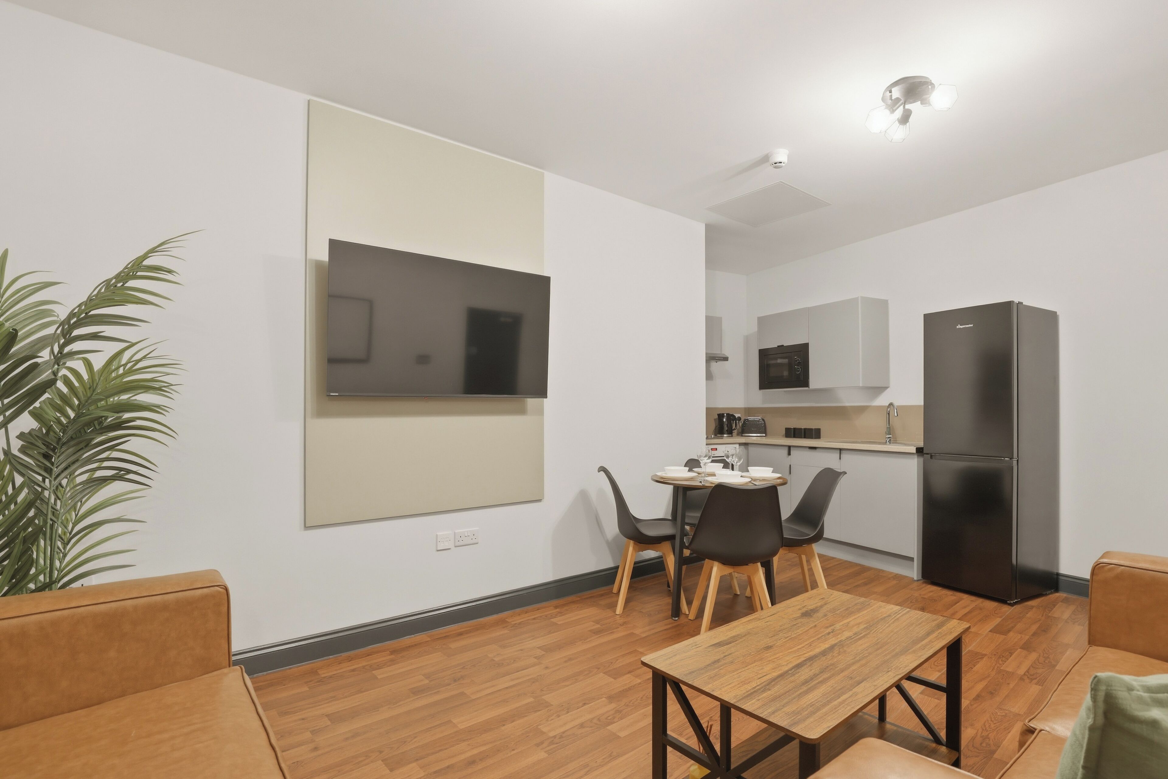 Una sala de estar moderna con una mesa y sillas de madera, un sofá, un espejo grande y una cocina al fondo.