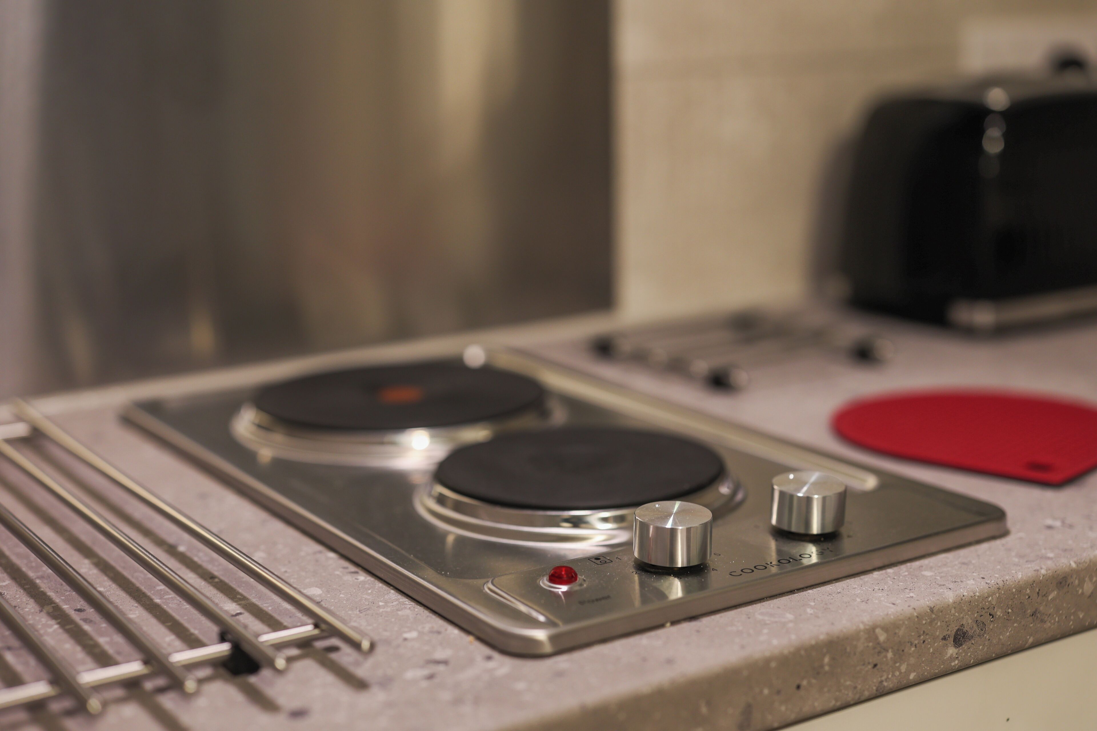 A kitchen with a stovetop, a red cutting board, and a stainless steel appliance.