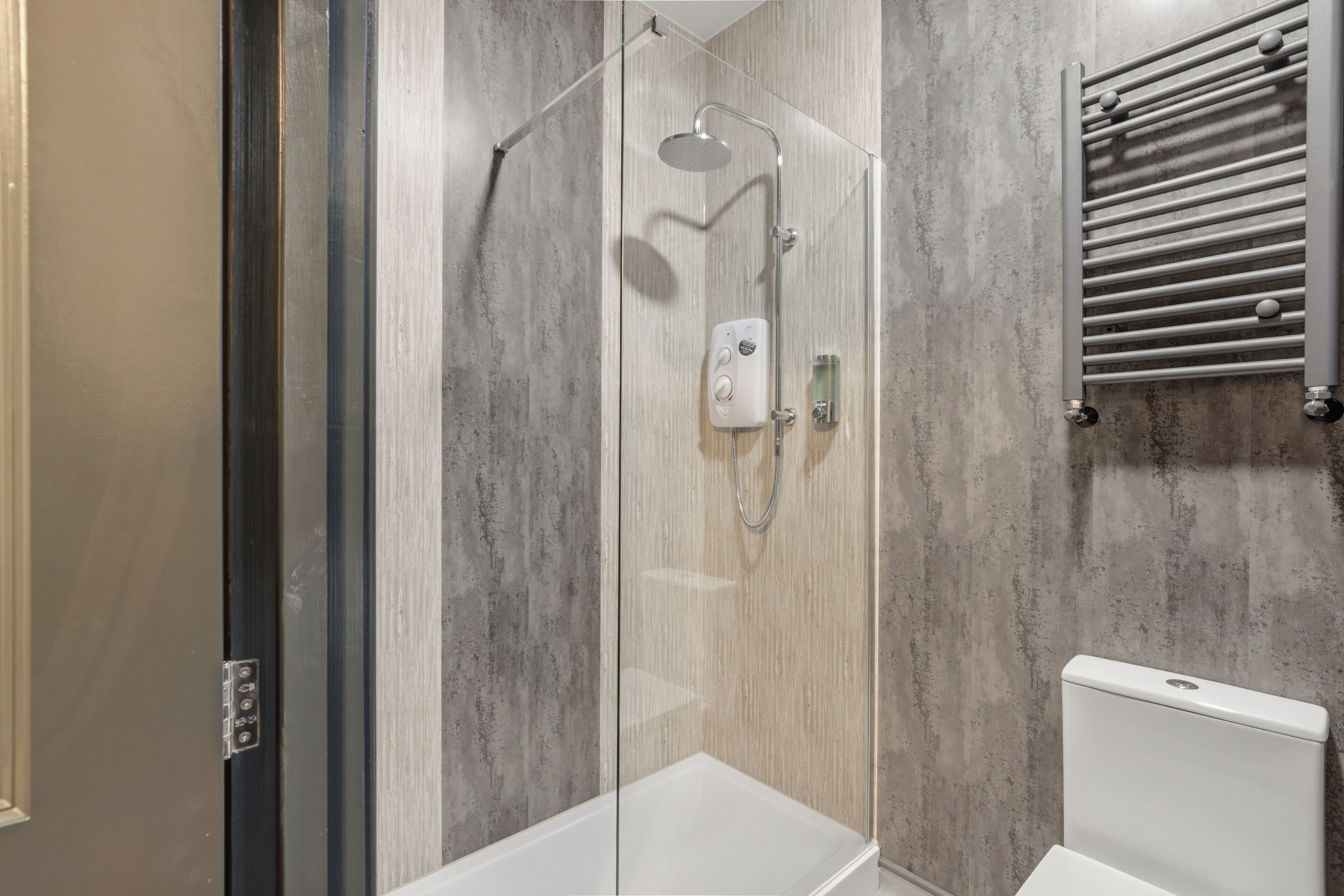 A modern shower enclosure with a glass door, a handheld showerhead, and a wall-mounted towel rack.