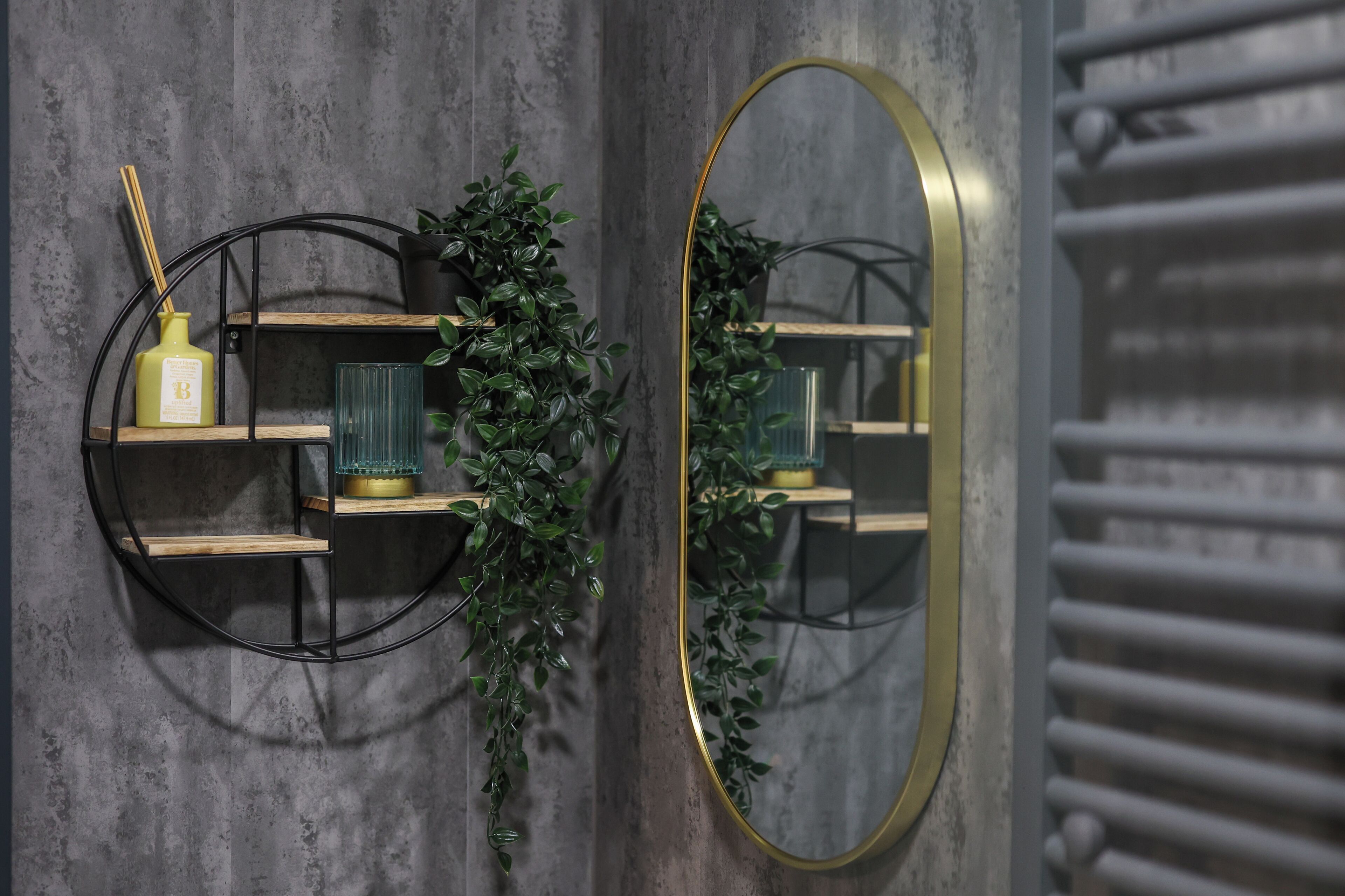 A wall-mounted mirror with a gold frame, a round shelf with a green vase, and a small potted plant.