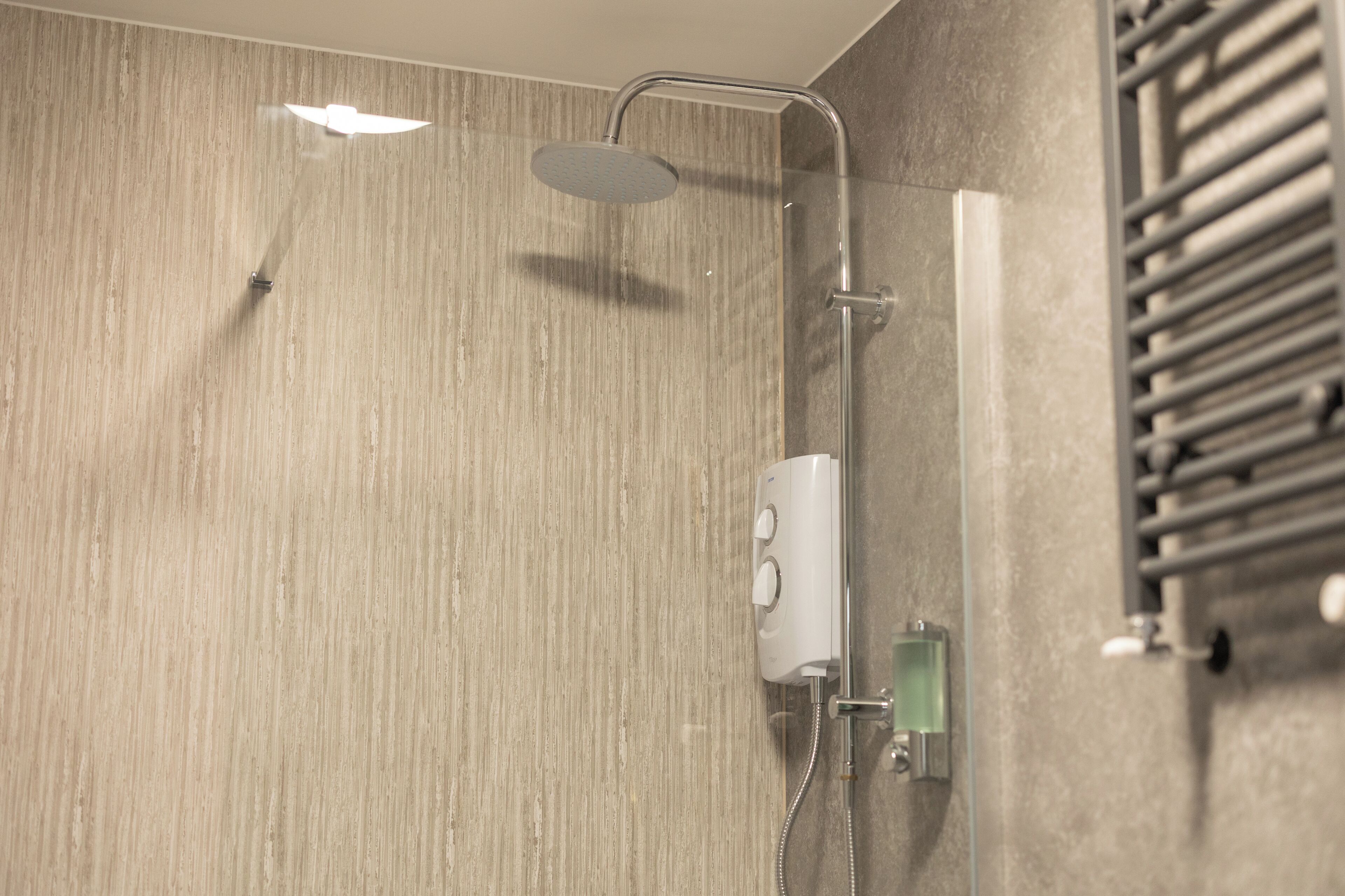 A modern shower with a handheld showerhead, a wall-mounted control panel, and a glass-enclosed soap dispenser.