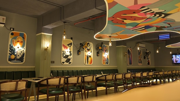 A restaurant with a long counter, green cushioned booths, and colorful wall art. - Hotel Spotlight  (Chatrapur)