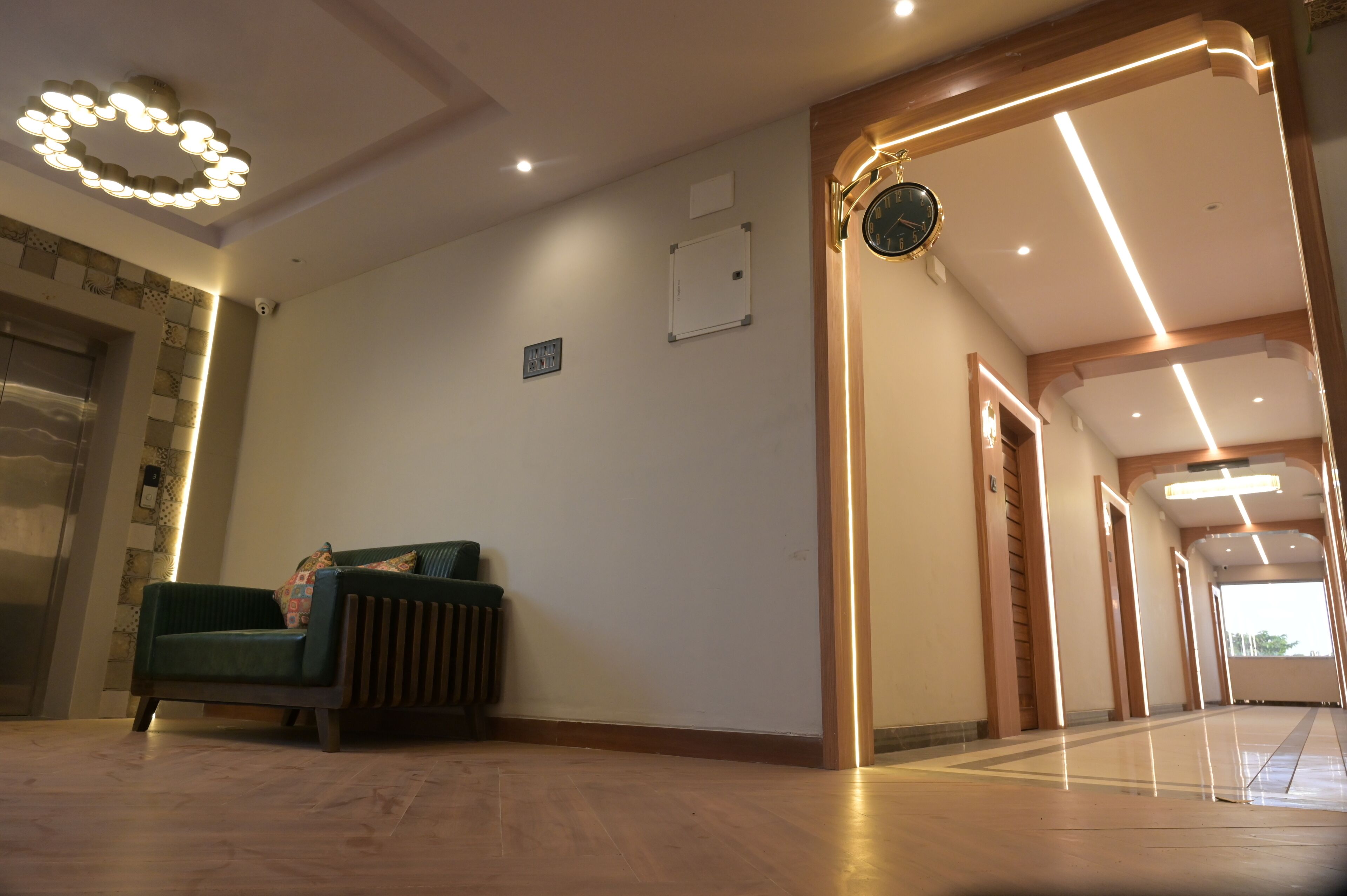 A modern hotel lobby with a green sofa, a clock, and a well-lit corridor.