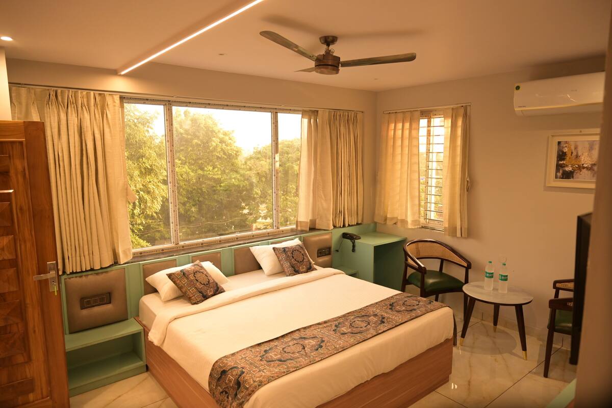 A bedroom with a large bed, a desk, a chair, and a small table with two bottles.