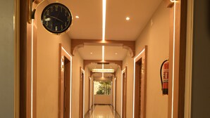 A long, well-lit hallway with a polished floor, a wall-mounted clock, and a fire extinguisher. - Hotel Spotlight  (Chatrapur)