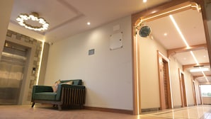 A hotel lobby with a green sofa, a clock, and a modern light fixture. - Hotel Spotlight  (Chatrapur)
