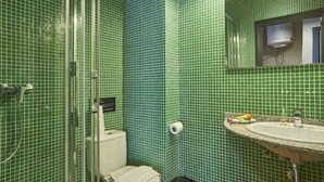 A bathroom with green mosaic tiles, a glass shower enclosure, a white toilet, and a sink with a mirror above it. - Spacious 2 bedroom apartment minutes from Ramblas -parking (Barcelona)