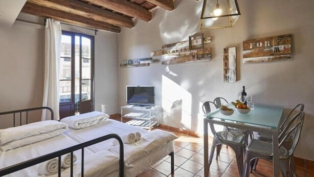 A room with a bed, a desk with a computer, a glass table with chairs, and a window with curtains. - Spacious 2 bedroom apartment minutes from Ramblas -parking (Barcelona)