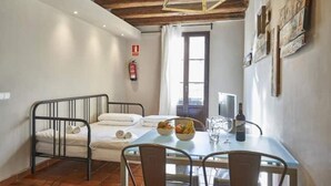 A room with a bed, a dining table with chairs, a window, and a fire extinguisher on the wall. - Spacious 2 bedroom apartment minutes from Ramblas -parking (Barcelona)