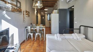 A compact room with a bed, a small table with chairs, a TV, and a kitchen area. - Spacious 2 bedroom apartment minutes from Ramblas -parking (Barcelona)