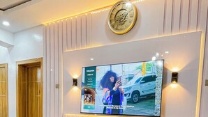 A modern living room with a flat-screen TV mounted on a wall, a marble coffee table, and a sofa. - La Veda Manor Luxury Apartment (Ibadan)