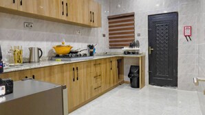 A modern kitchen with wooden cabinets, a stainless steel refrigerator, and a black door. - La Veda Manor Luxury Apartment (Ibadan)