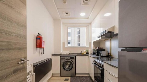 A compact kitchen with a washing machine, oven, and a small window. - High floor 1BR vacation home with terrace (Dubai)