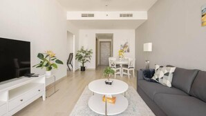 A modern living room with a flat-screen TV, a grey sofa, a white coffee table, and a dining area with a white table and chairs. - High floor 1BR vacation home with terrace (Dubai)