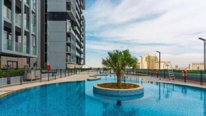 A modern building with a swimming pool, palm trees, and a clear sky. - High floor 1BR vacation home with terrace (Dubai)