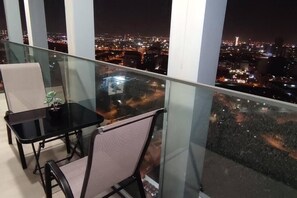 Ein Balkon mit Glastisch und Stühlen, mit Blick auf eine nächtliche Stadtlandschaft.
