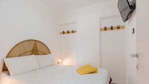 A neatly made bed with white bedding and a yellow pillow, a wall-mounted TV, and a wooden shelf with hooks. - Pino Baroque near Beach & Etna by Wonderful Italy (Catania)