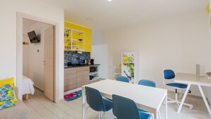 A modern, well-lit room with a dining table, chairs, a kitchen area with a microwave and coffee maker, and a bed with a colorful pillow. - Pino Baroque near Beach & Etna by Wonderful Italy (Catania)
