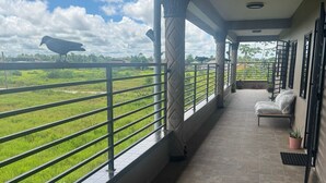 A covered balcony with a view of a green field and a bird in the distance. - Sisa Omi Appartments (Lelydorp)